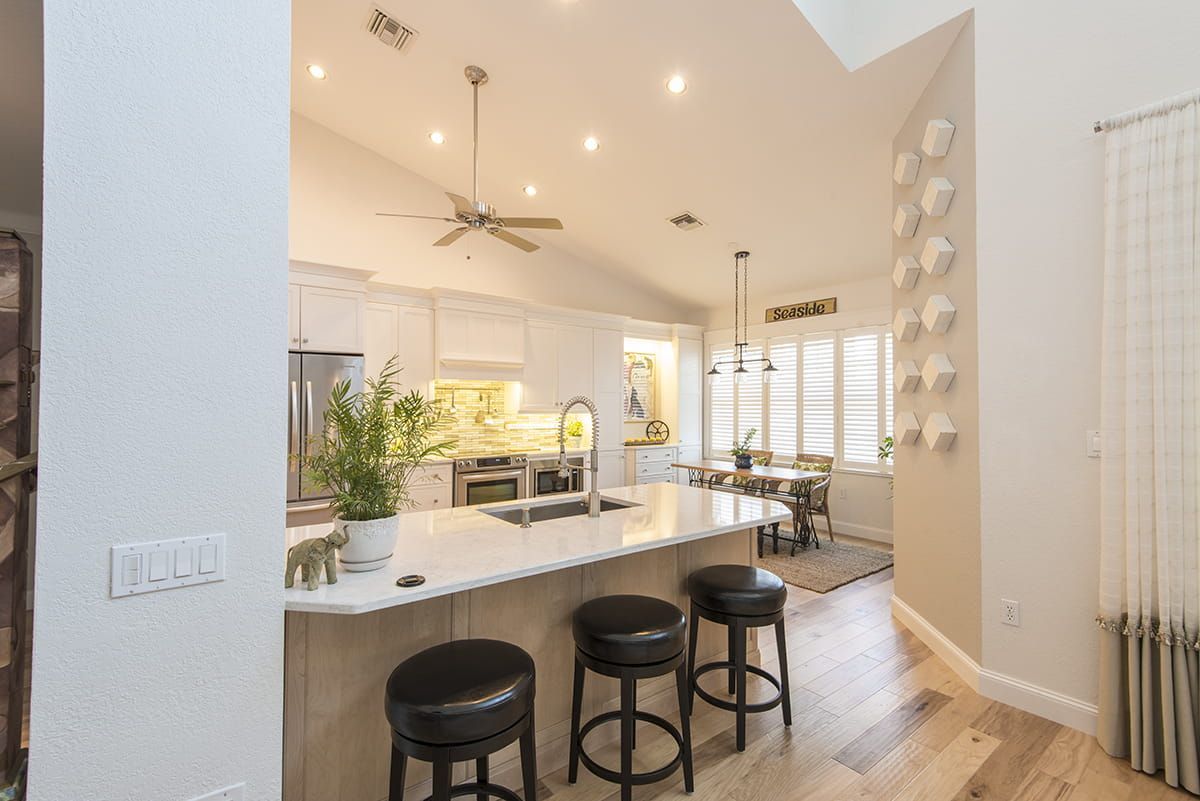 Bright open kitchen with marble island, black stools, and high ceilings with recessed lights