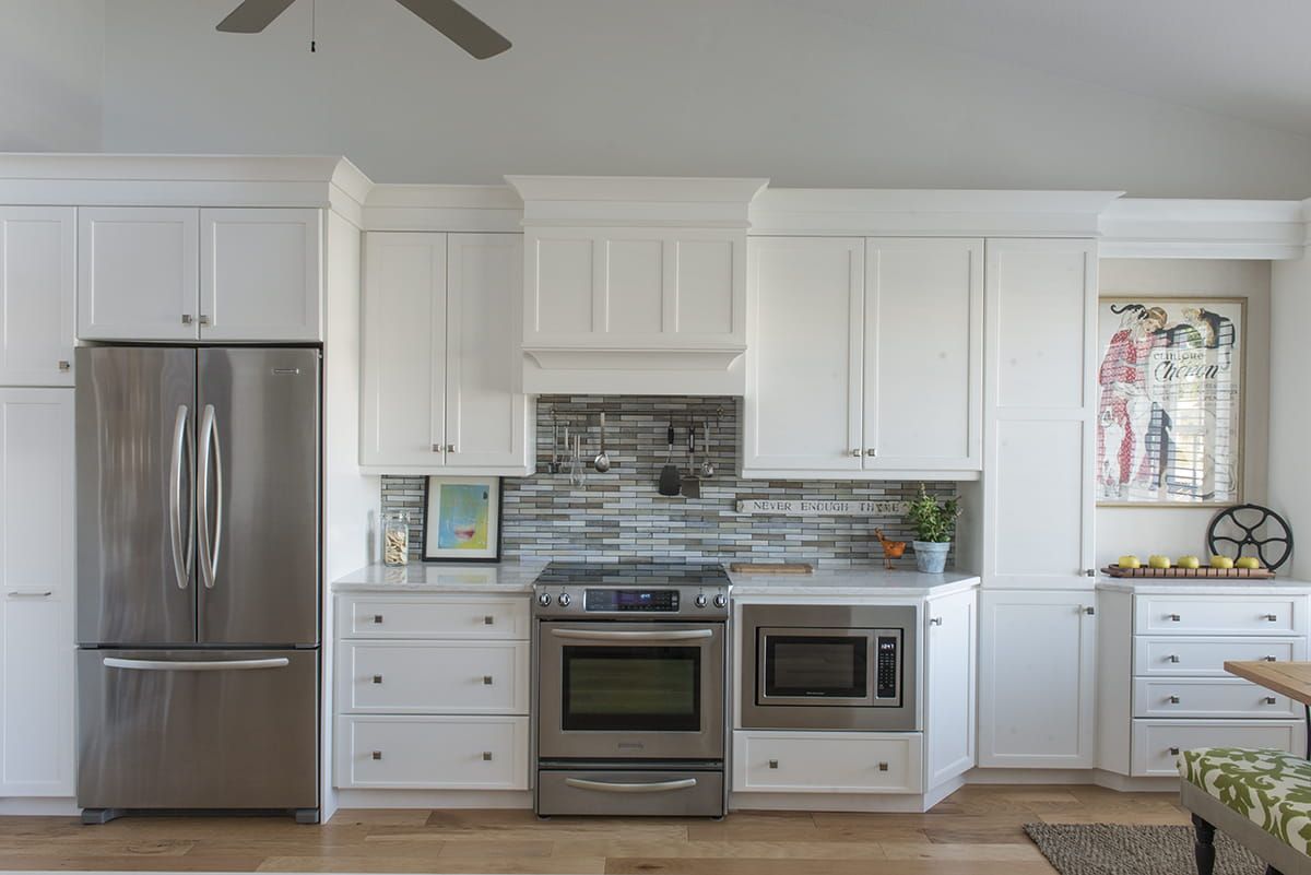 Modern white kitchen with stainless steel refrigerator, oven, and blue-gray tile backsplash