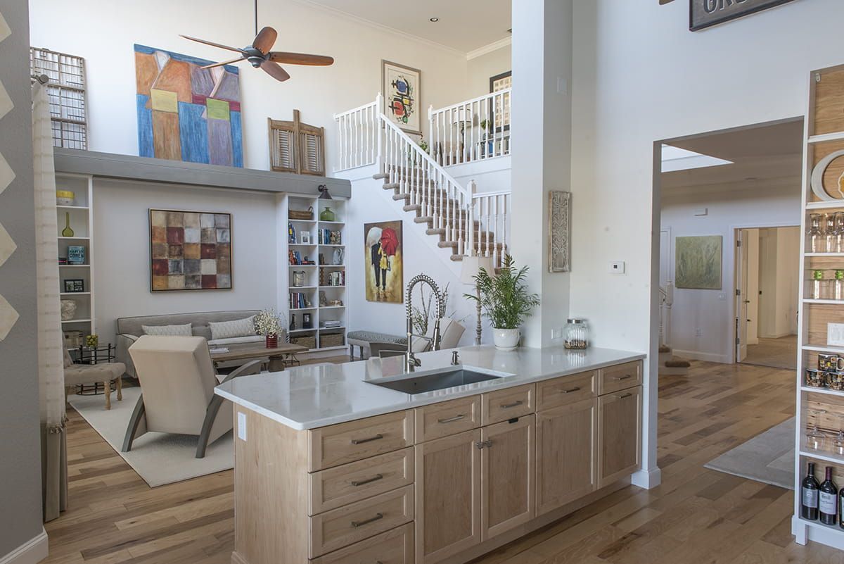 Bright open kitchen and living area with island, staircase, and loft artwork