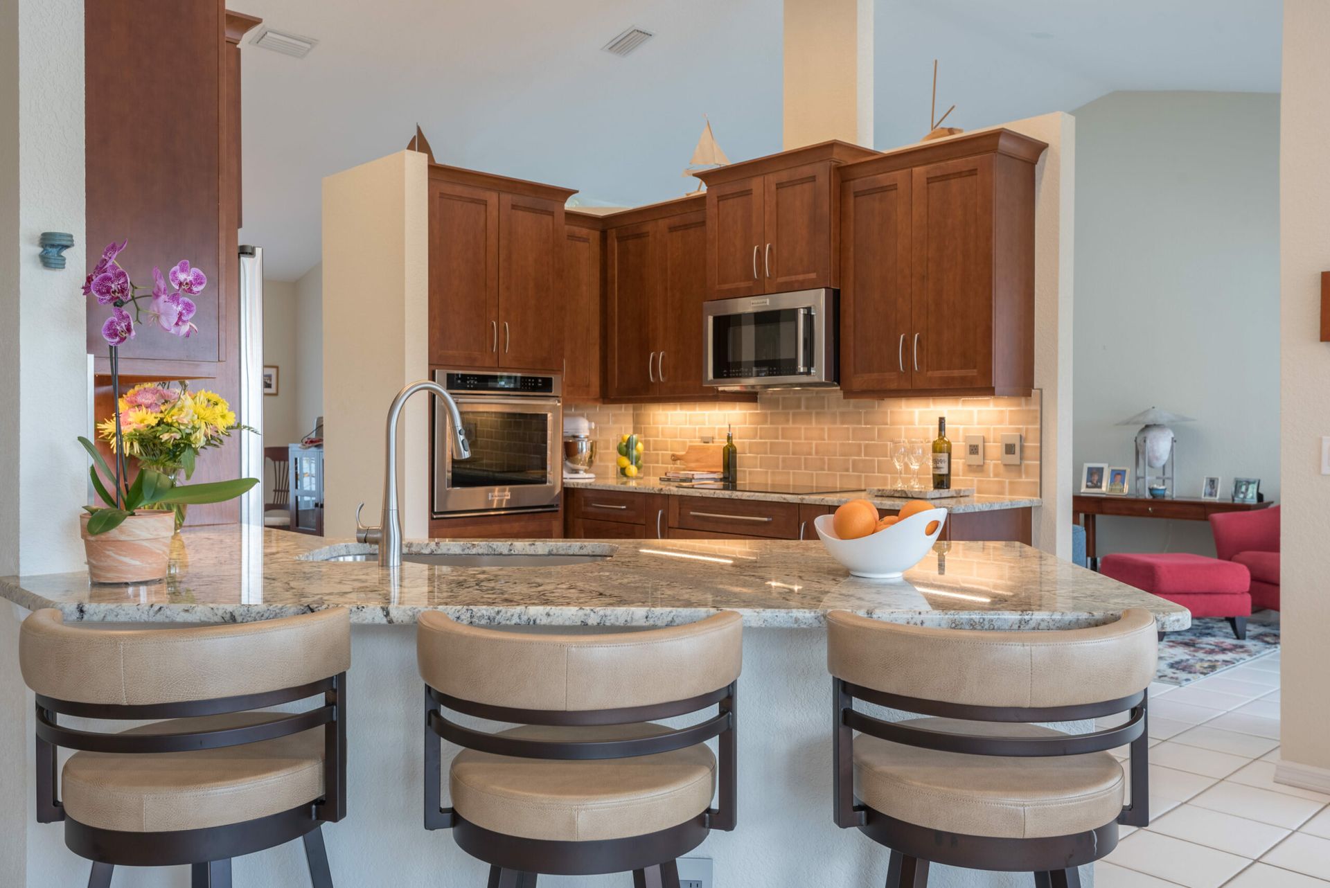 Modern kitchen with wood cabinets, granite island, and bar stools, with an adjacent living area.
