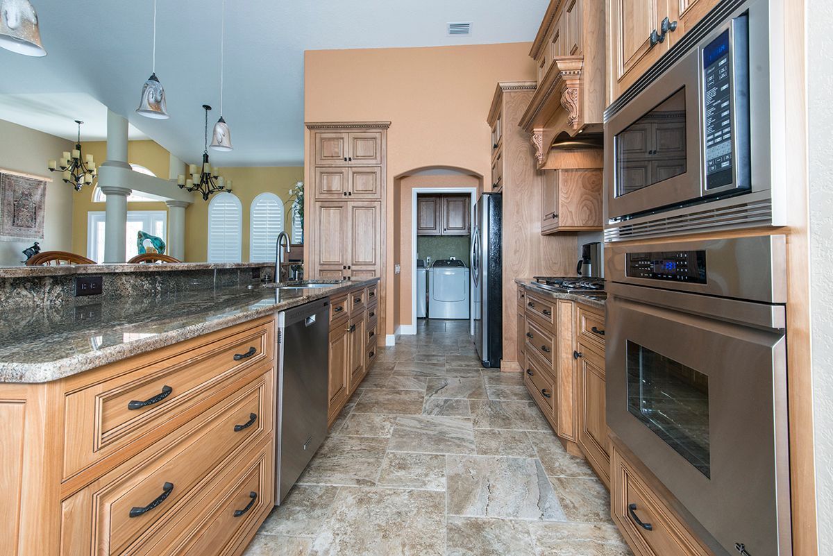Modern kitchen with granite counters, wood cabinets, stainless steel appliances, and tiled floor