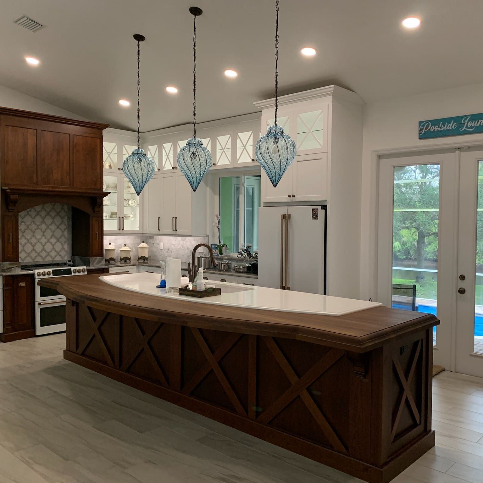 Bright modern kitchen with wood island, white cabinets, pendant lights, and glass doors to outside.