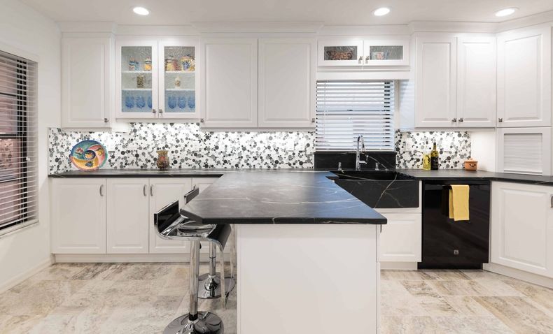 Bright white kitchen with black countertops, island, and patterned backsplash.
