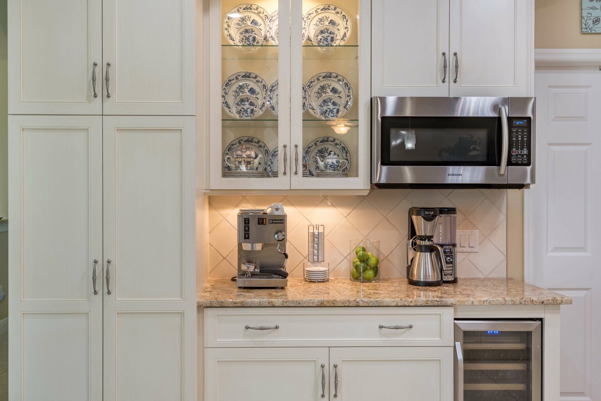 Bright kitchen with white cabinets, glass-front shelves, granite counters, microwave, and coffee maker