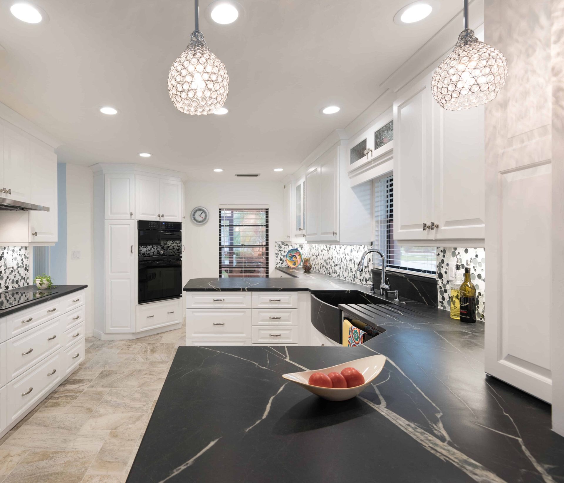 Bright modern white kitchen with black countertops, pendant lights, and a bowl of fruit on the island