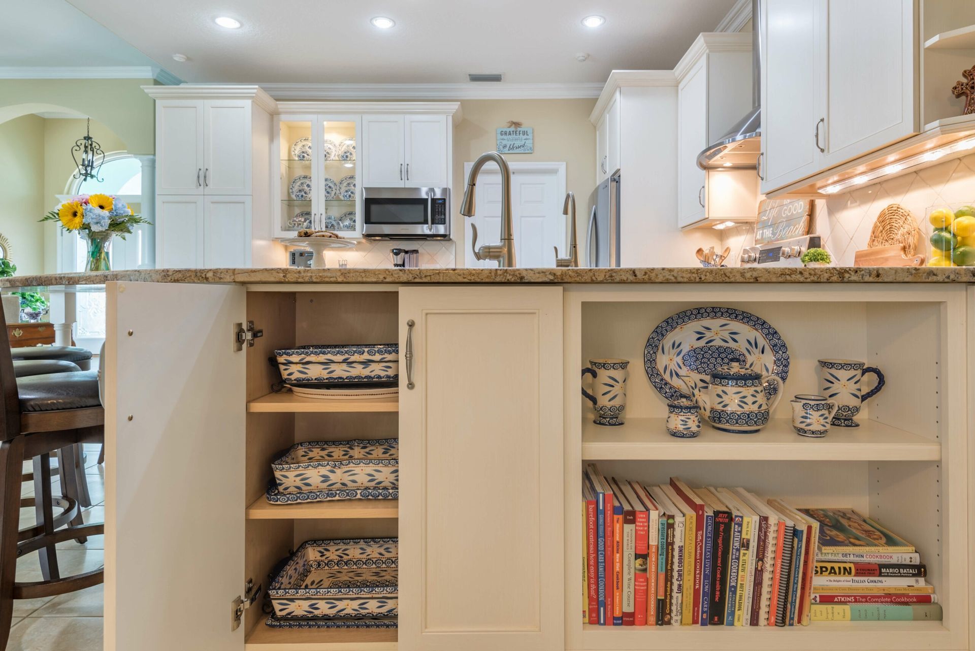 Kitchen remodeling in Punta Gorda, FL, bright kitchen with white cabinets, island sink, open shelving, blue dishes, and cookbooks on display