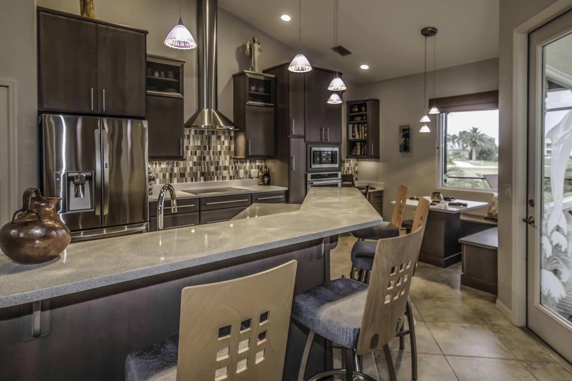 Modern kitchen with dark cabinets, stone island, pendant lights, and a dining area by large windows