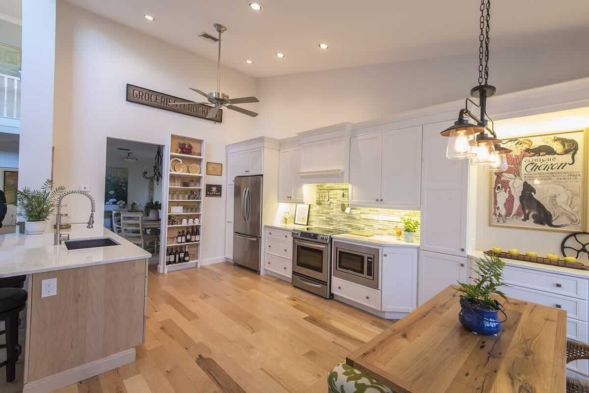 Bright modern kitchen with white cabinets, wood floors, island, pendant lights, and a wooden dining table
