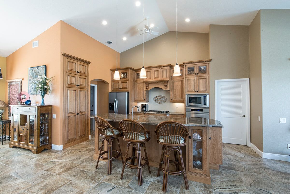 Kitchen remodeling in Punta Gorda, FL, open-plan kitchen with wood cabinets, granite island, barstools, and bright modern interior layout