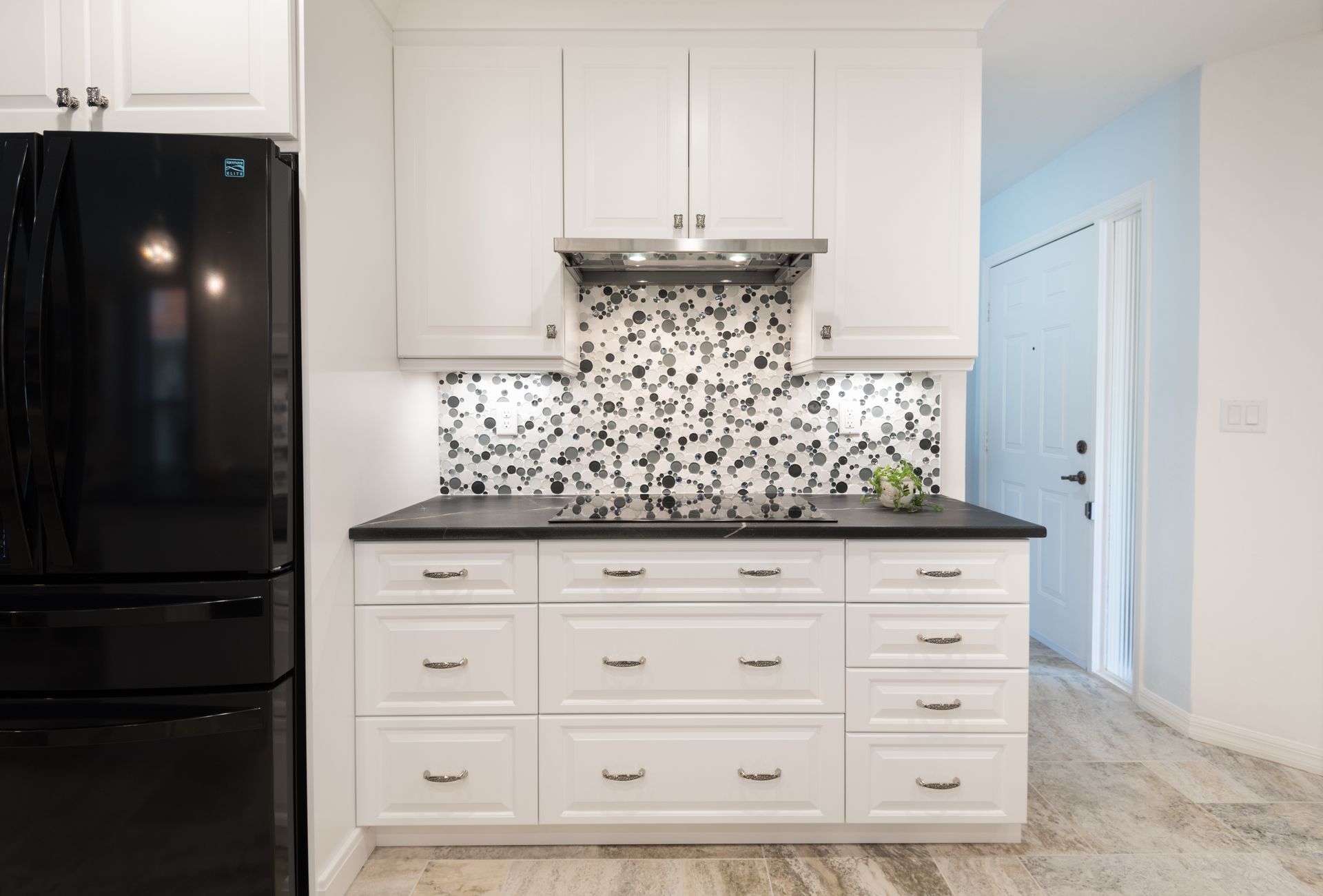 Kitchen remodeling in Punta Gorda, FL, bright white kitchen with black refrigerator, patterned tile backsplash, and white cabinets with dark countertop.