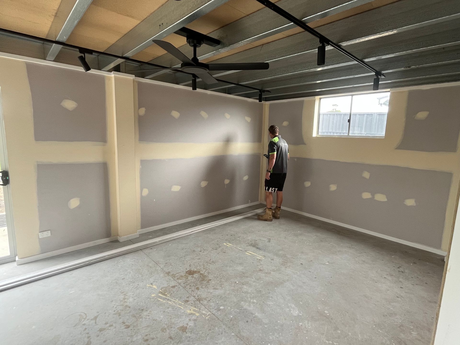 A man is standing in an empty room with a ceiling fan — TM Built Construction In Lochinvar, NSW