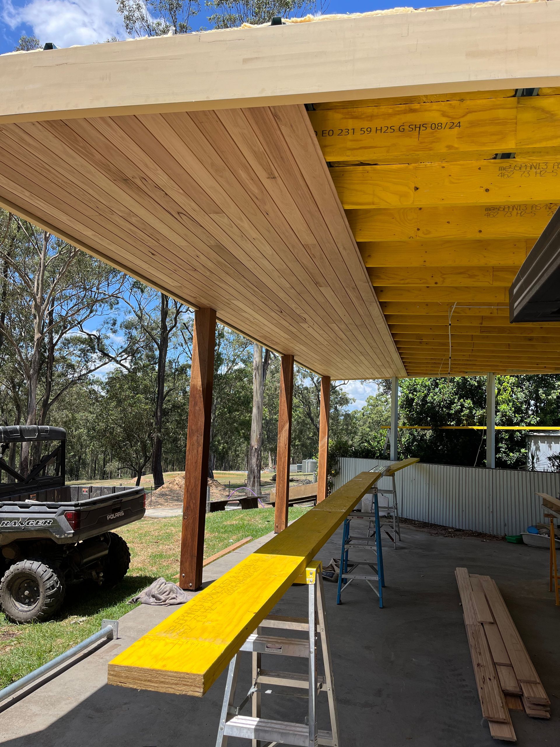 A yellow plank is sitting under a wooden roof — TM Built Construction In Lochinvar, NSW