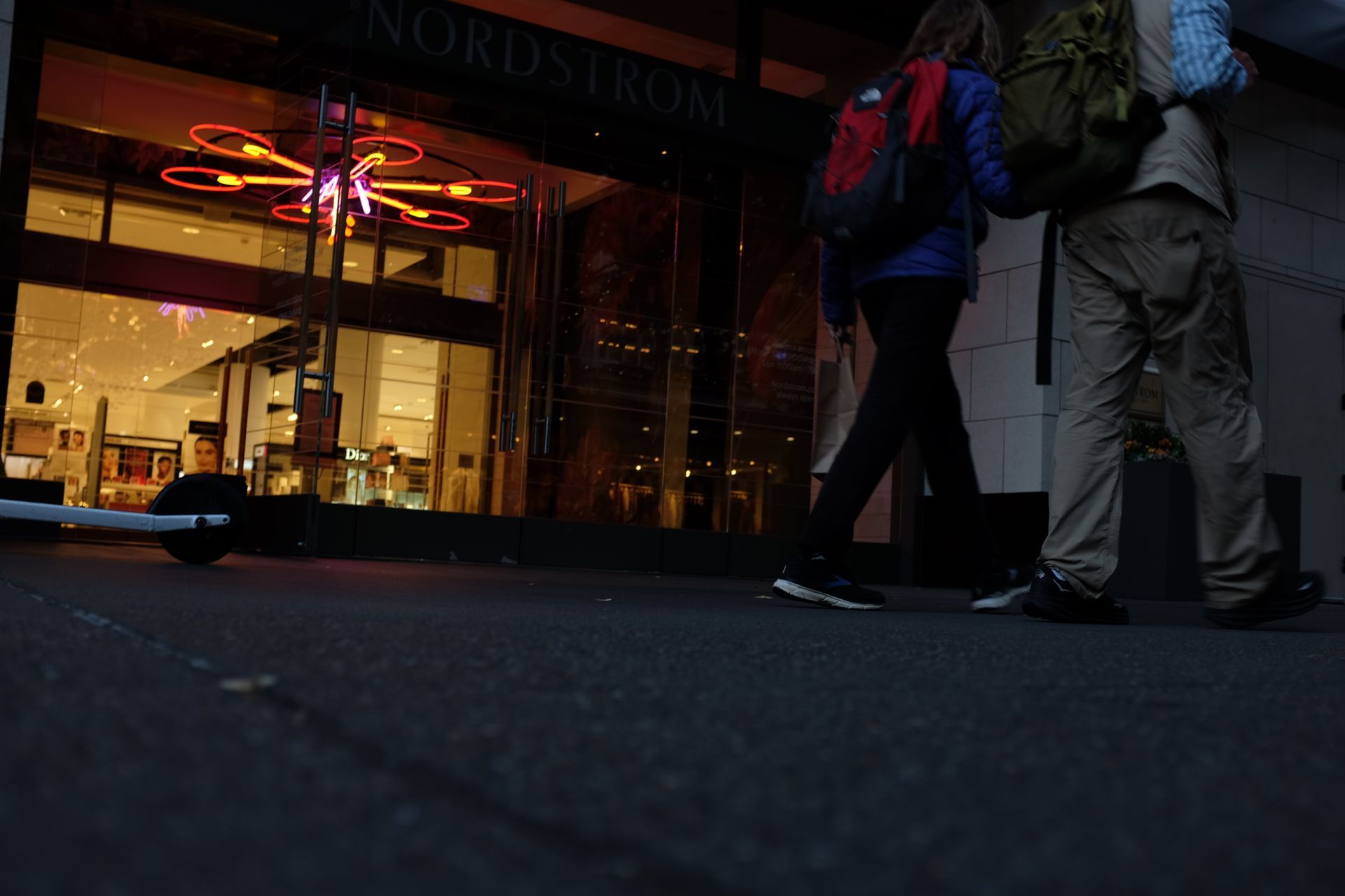 People walking past a Nordstrom store at night, a decorative light fixture above the entrance; art by Yale Wolf. 