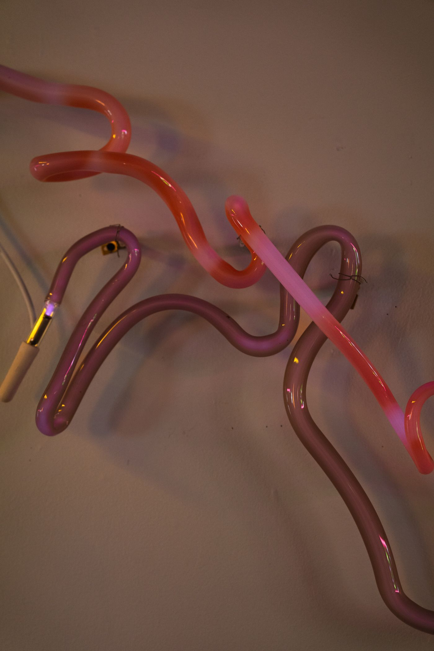 Pink and purple neon light sculpture on a tan wall.