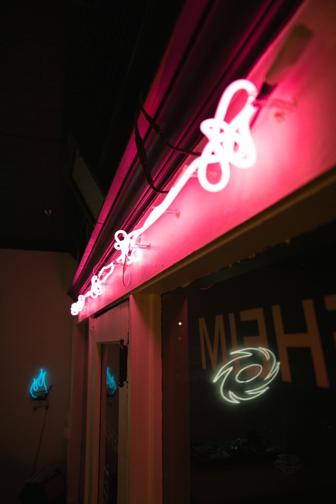 Pink neon lights by Yale Wolf above a glass door; a white logo is reflected on the glass.