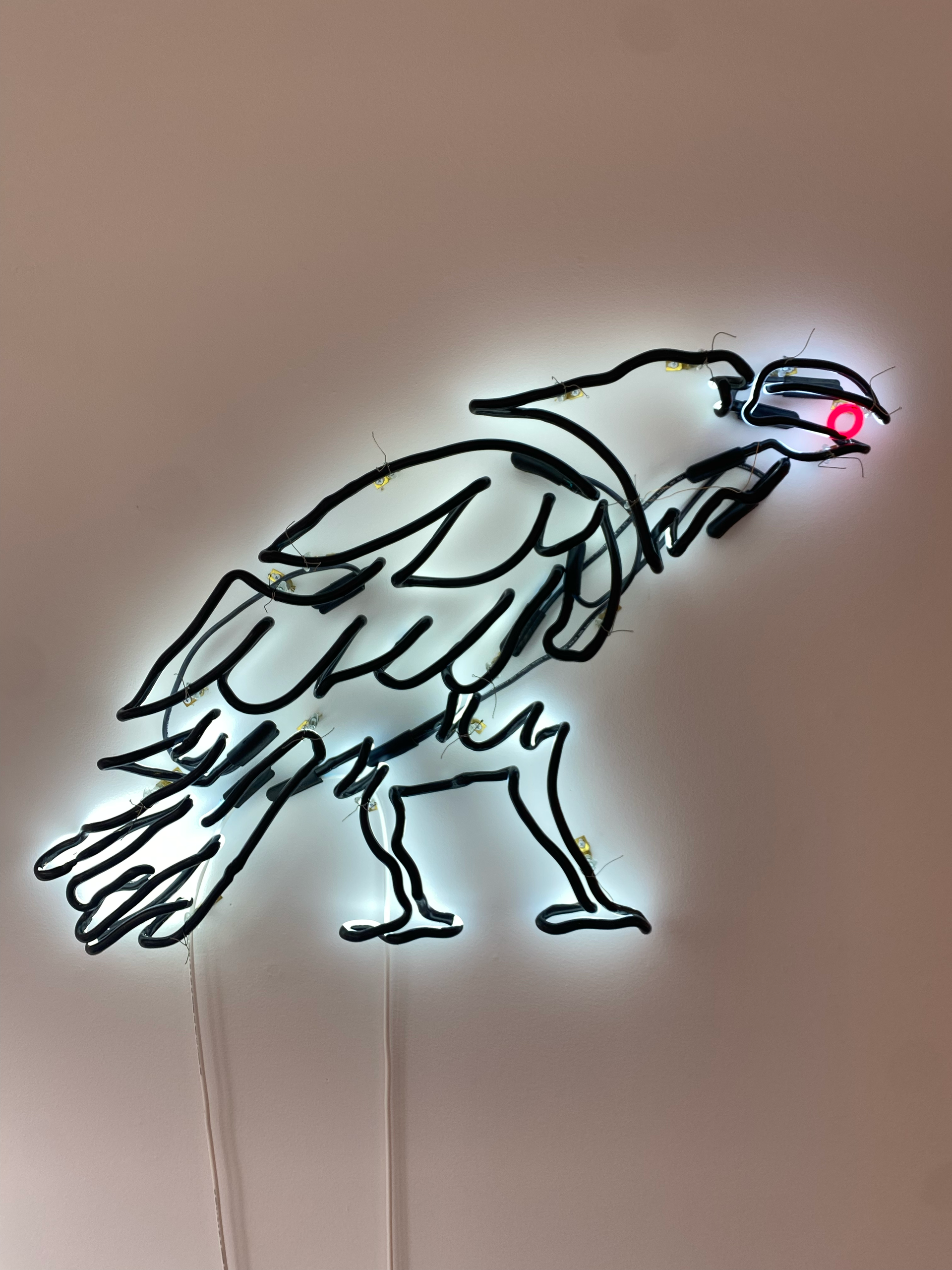 Neon eagle outline, black with white glow, red eye, mounted on a light wall; by Yale Wolf.