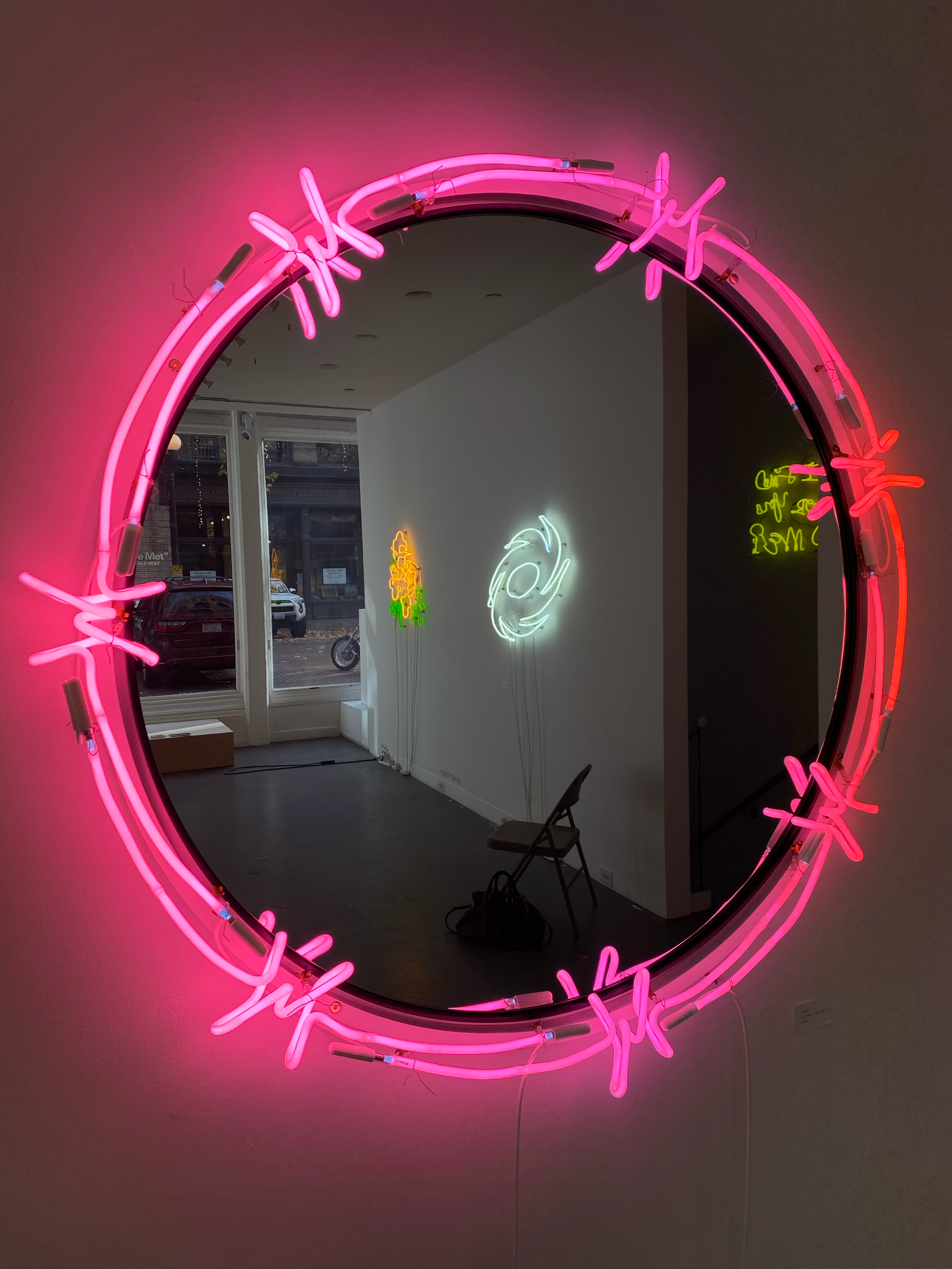 Pink neon circle sculpture by Yale Wolf with barbed wire detail, reflecting a gallery interior with neon art.