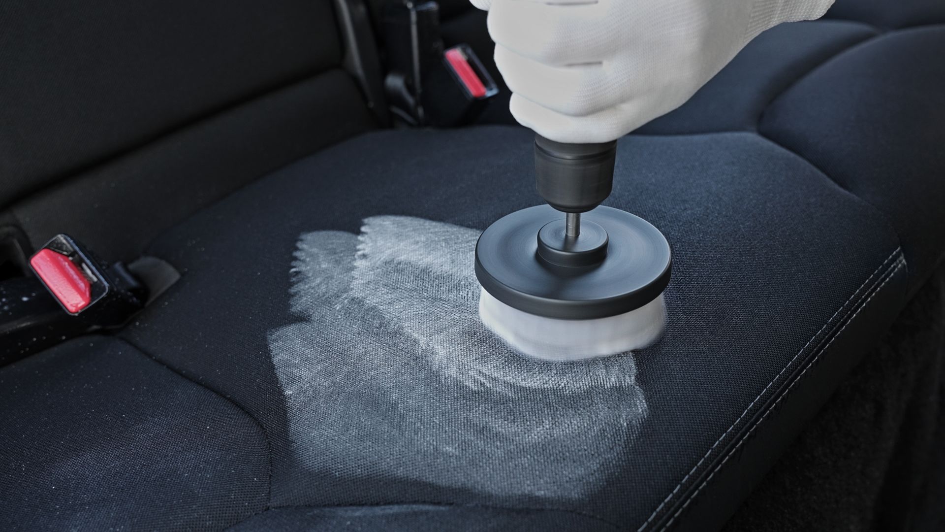 A drill with a polishing pad cleaning a gray car seat inside a vehicle