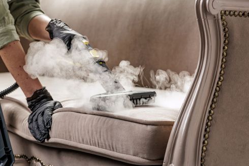 Person removing stuffing from a beige upholstered sofa with gloved hands