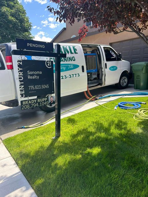 White van parked by a house with its side door open, next to a black parking sign and green lawn.