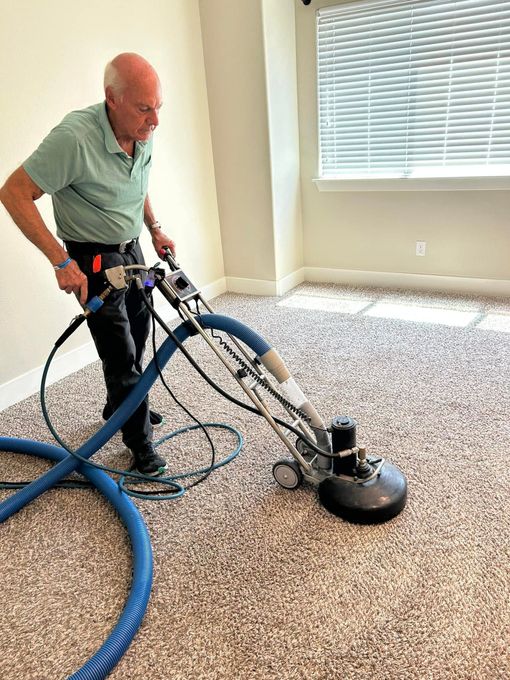 Man operating a floor buffer in a carpeted room near a window with blinds