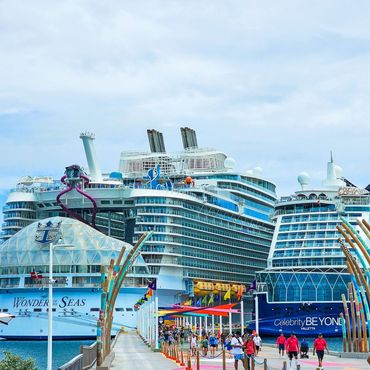 Cruise ships docked at a pier; people walking by, blue sky, bright colors.