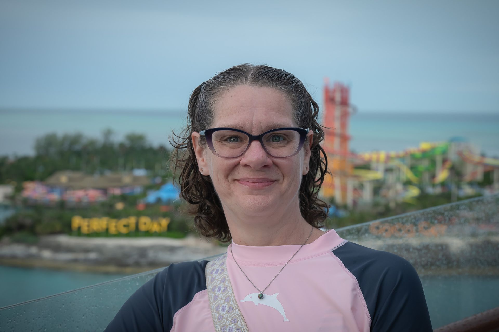 Woman with glasses smiling, standing on a deck with a water park and