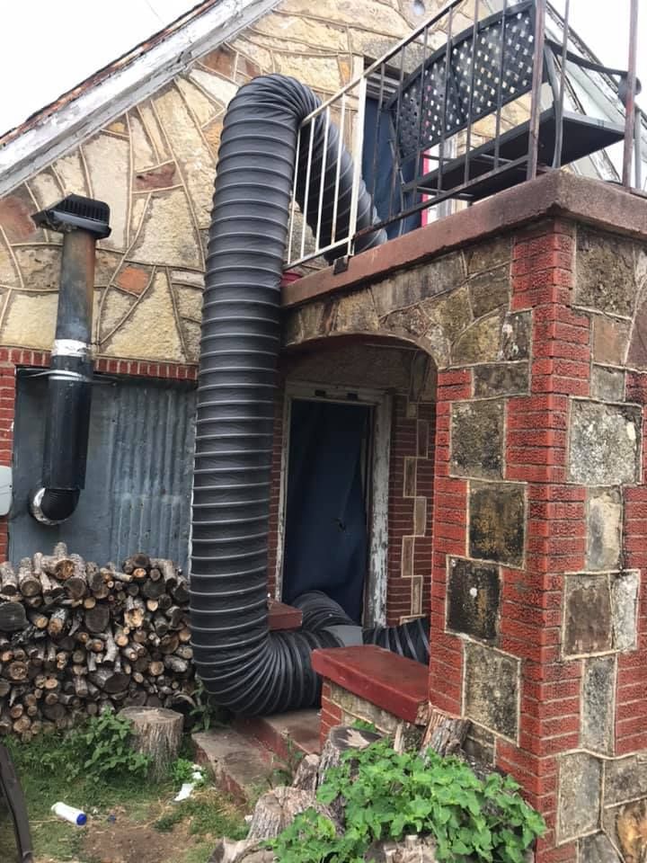 A large black hose is attached to the side of a brick building.
