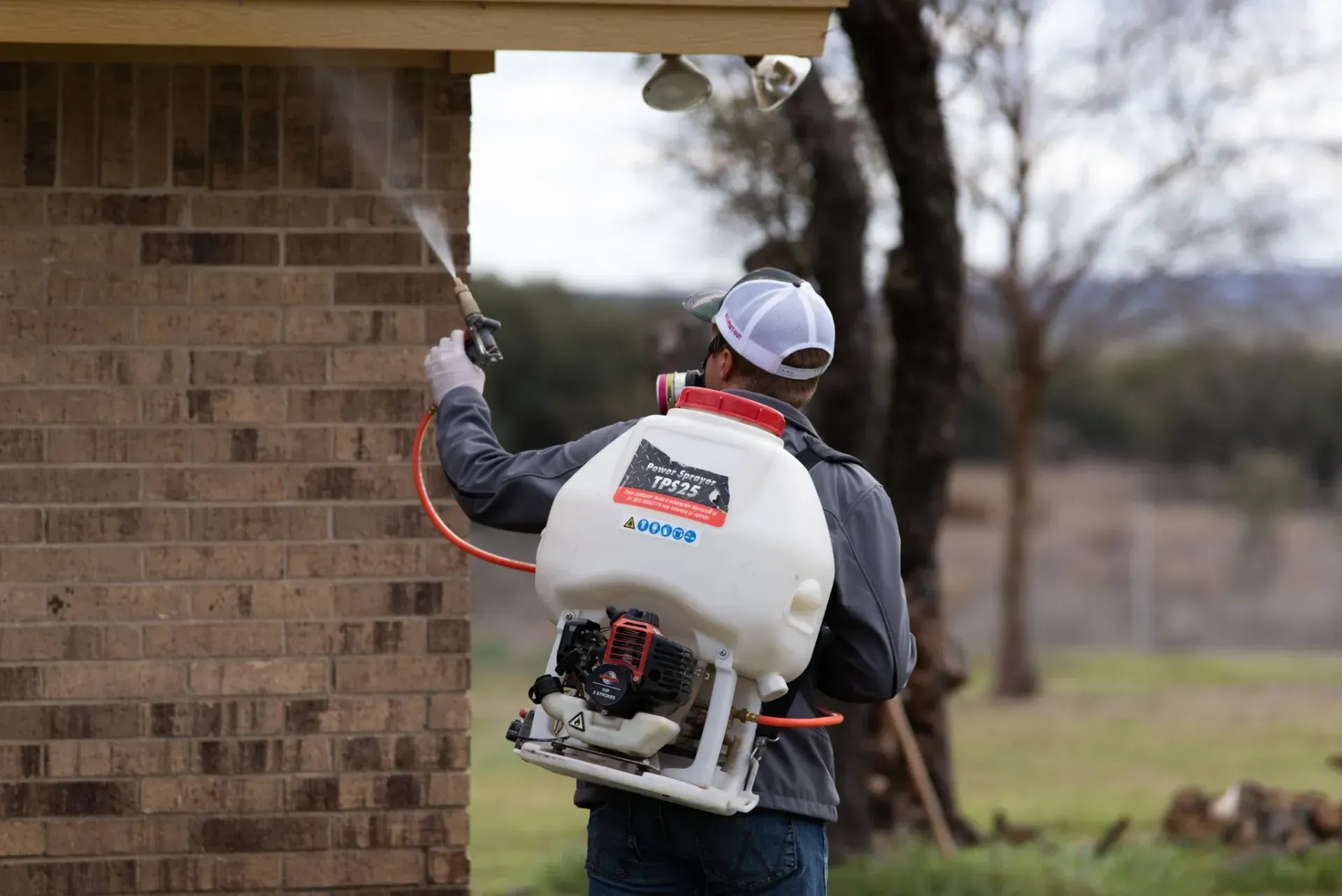A man is spraying a brick wall with a backpack sprayer.