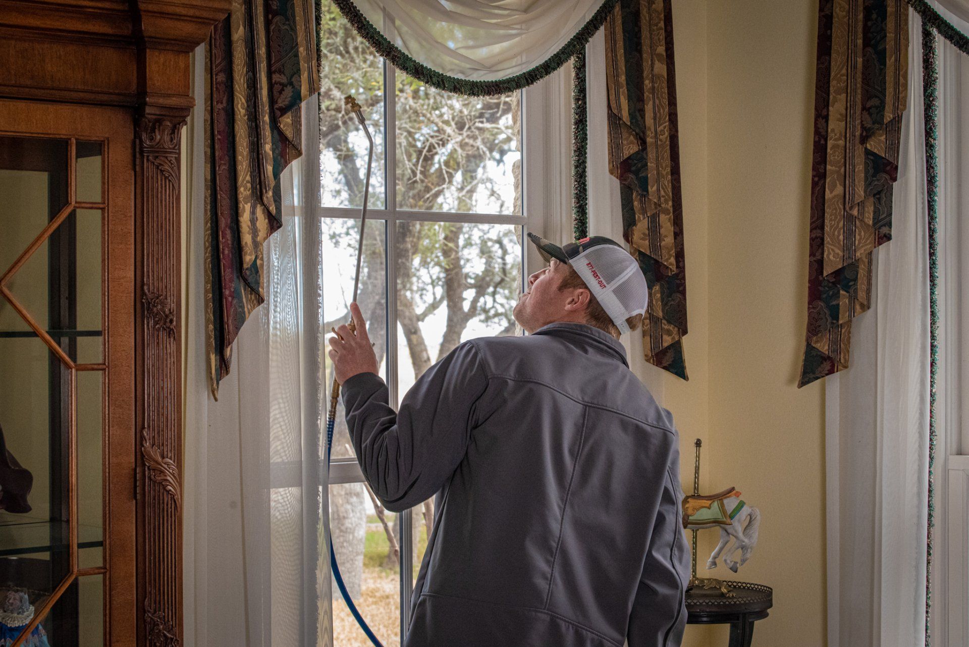 A man is cleaning a window with a hose in a living room.