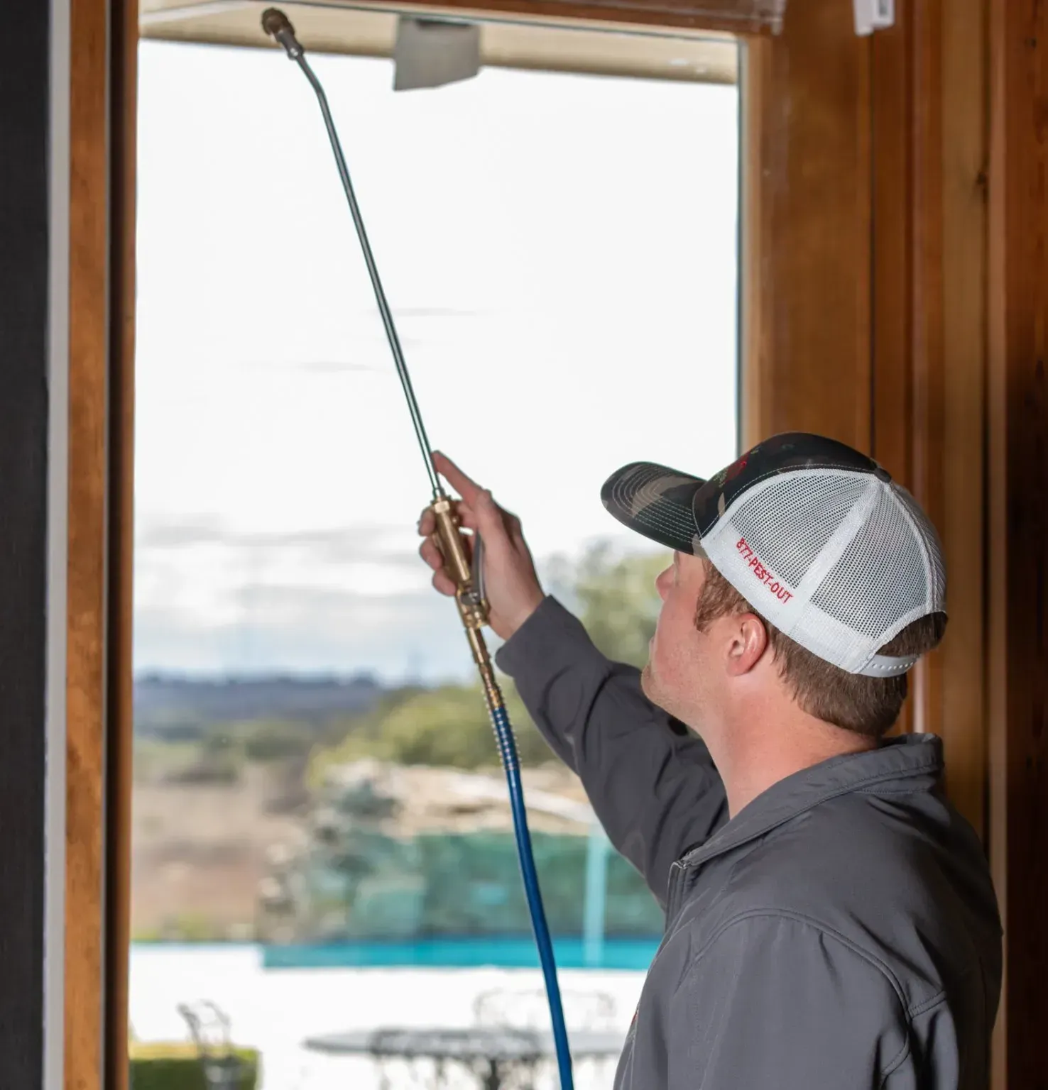 A man wearing a wilson hat is spraying a window