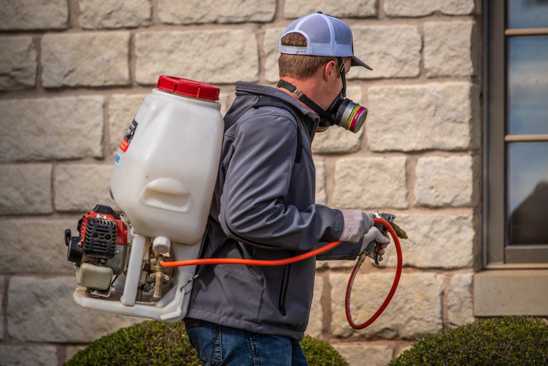 A man is spraying a brick wall with a backpack sprayer.