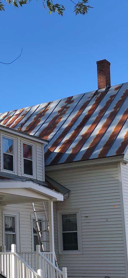 A white house with a rusty tin roof and a chimney.