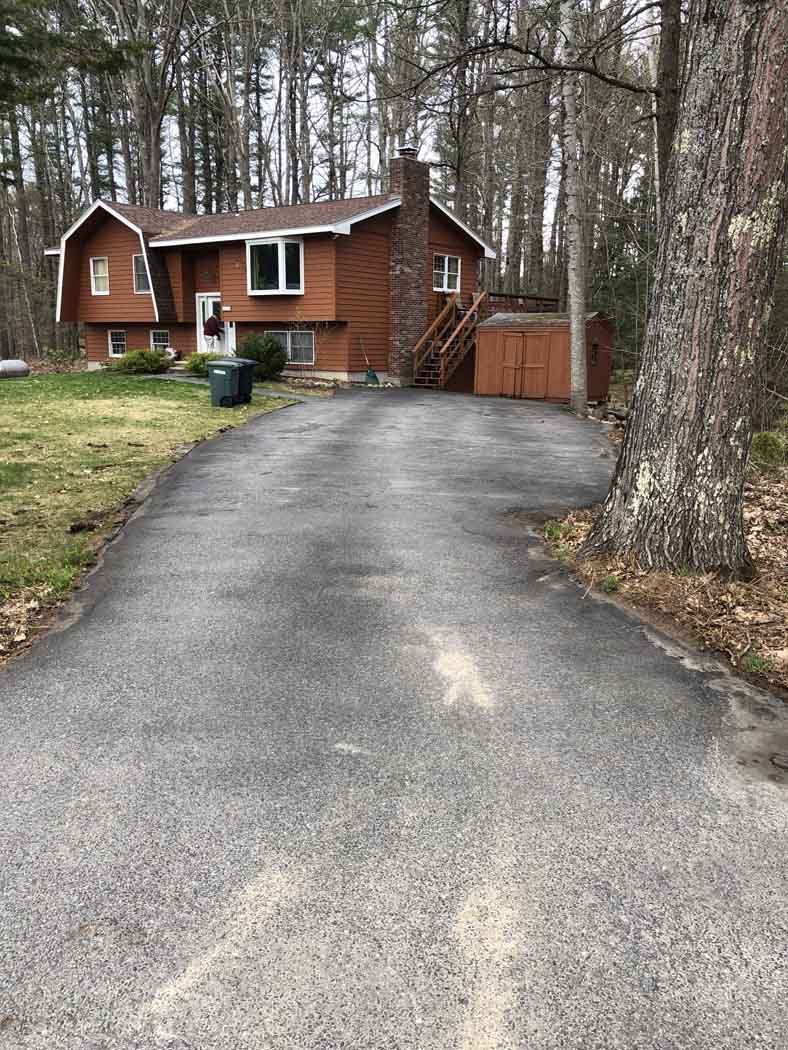 A driveway leading to a large red house surrounded by trees.