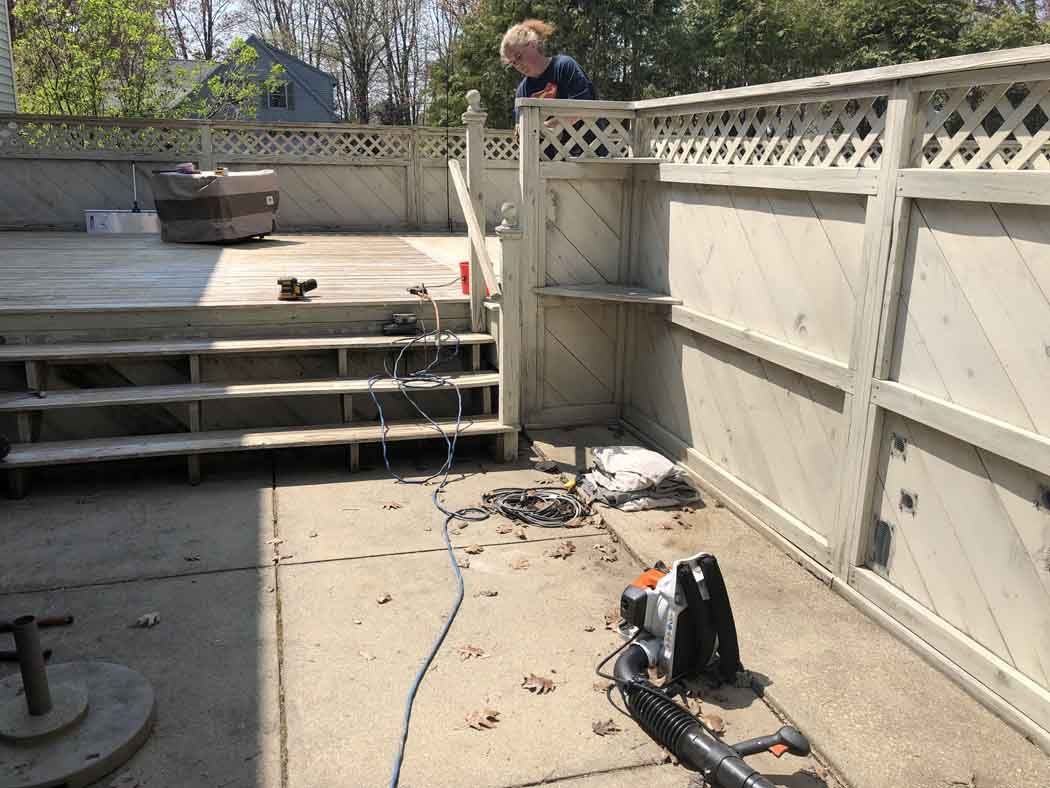 A man is standing on top of a wooden fence next to a vacuum cleaner.