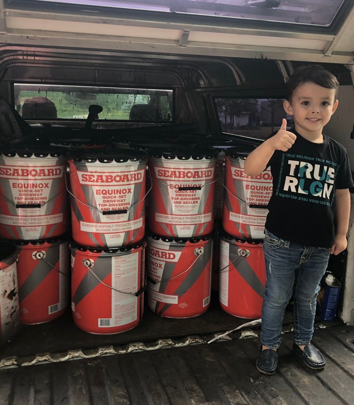 A smiling child in a black t-shirt and jeans stands in a truck bed next to several red and white Seaboard buckets.