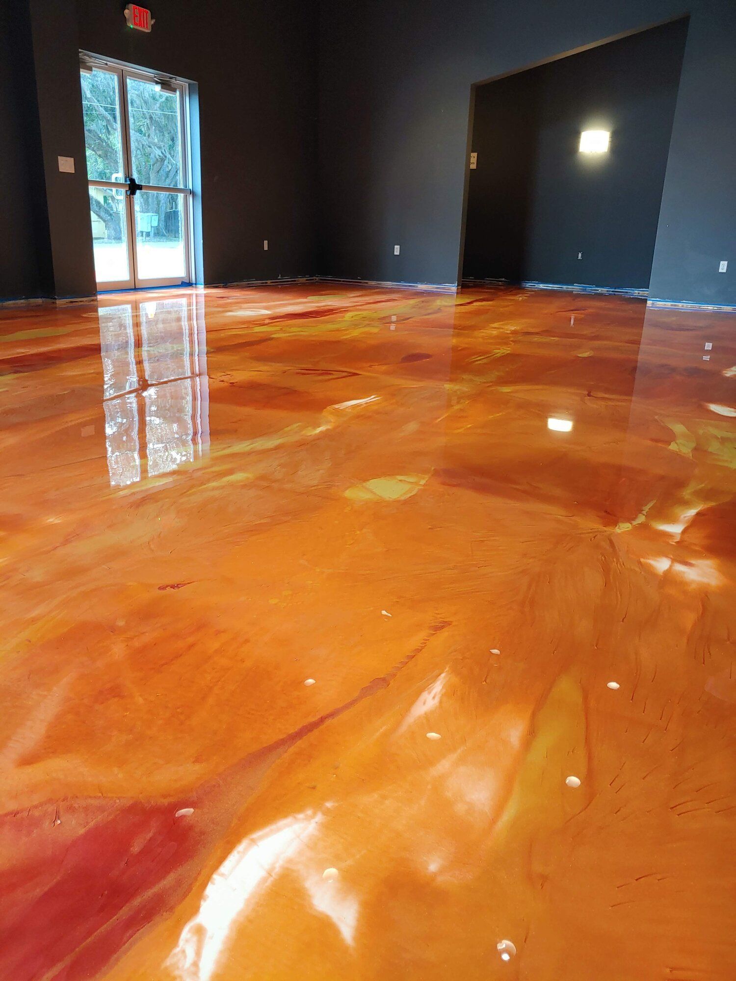 Glossy orange epoxy floor in a dark empty room with a window and doorway reflected in the surface