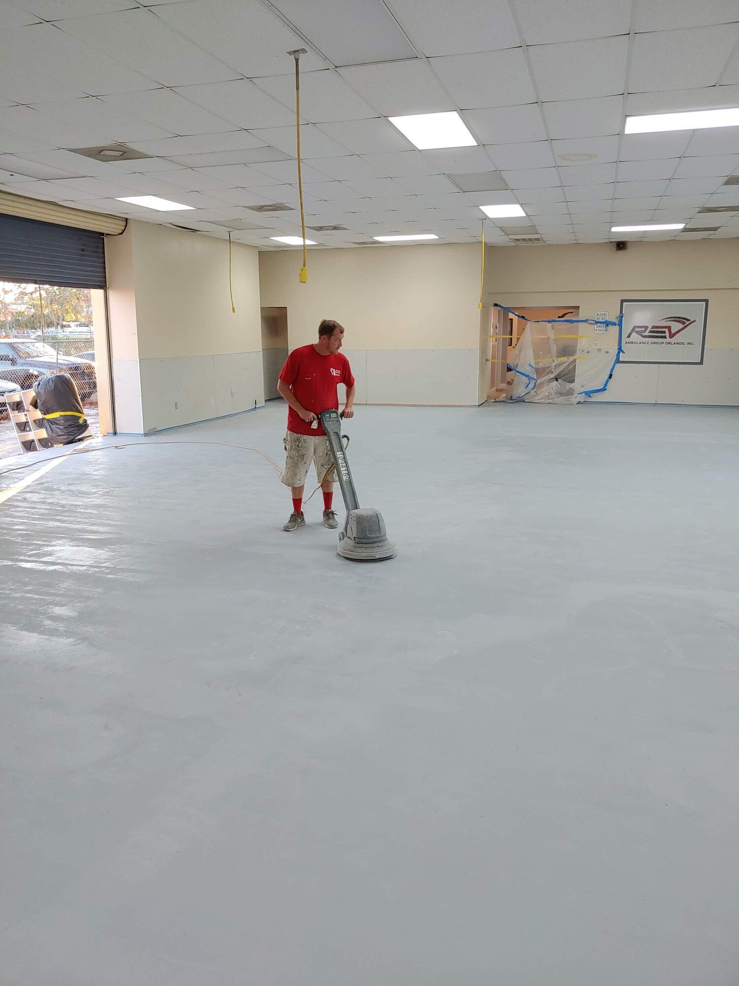 Person using a floor polishing machine in an empty storefront with a light gray floor.