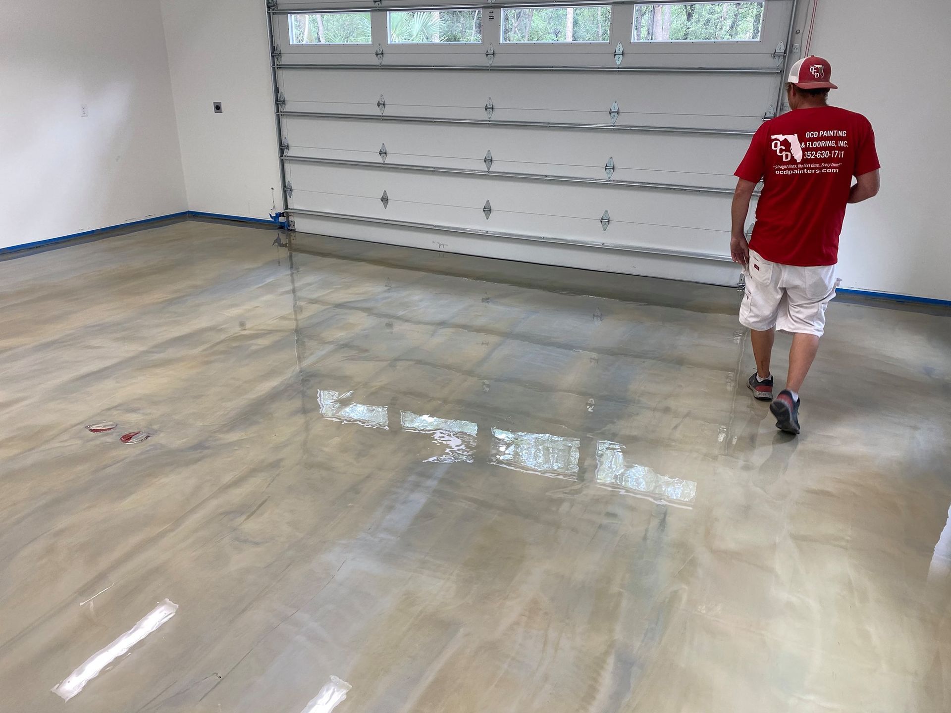 Person in a red shirt walking across a shiny garage floor near a closed garage door.