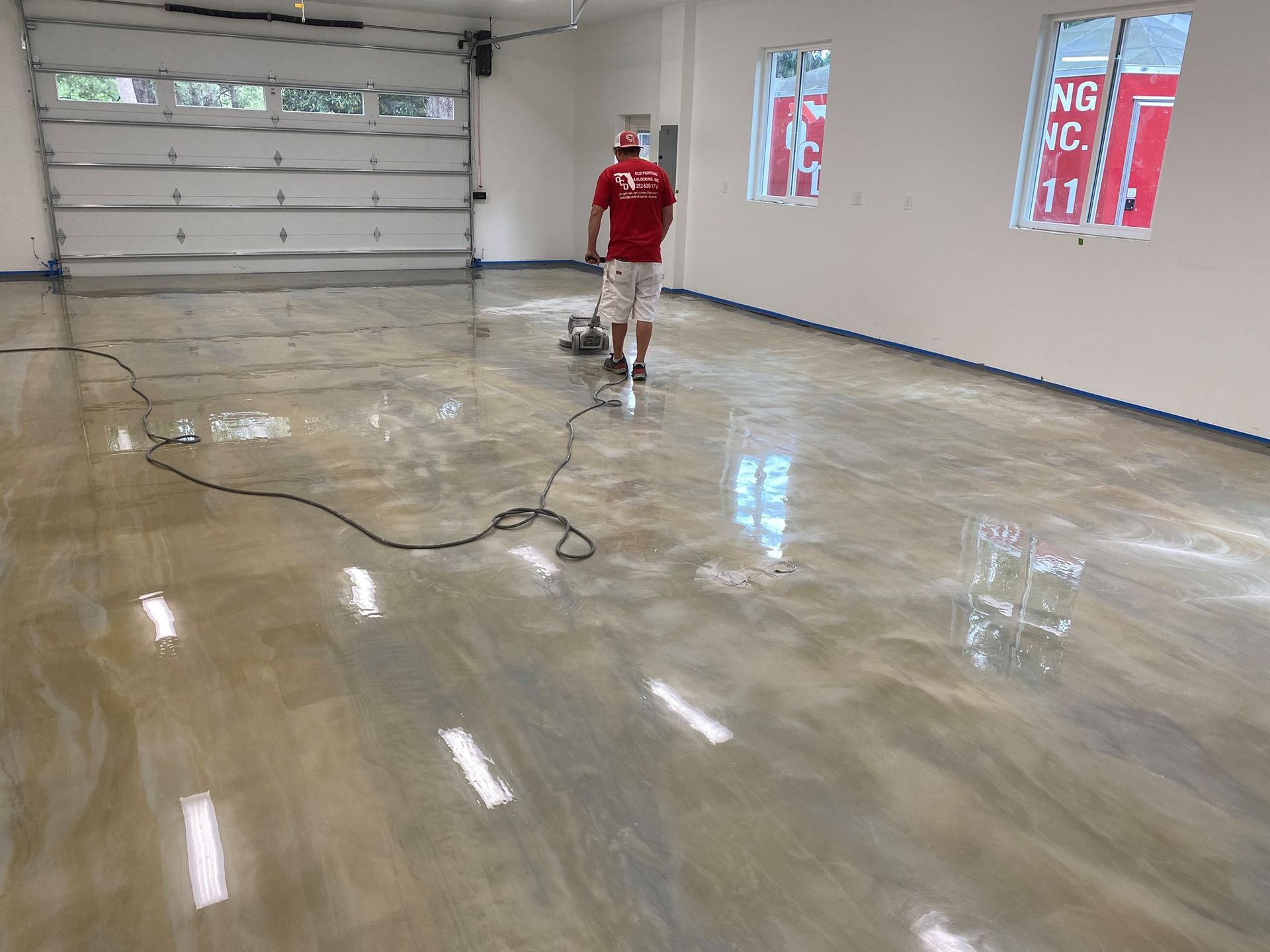 Person in a red shirt and shorts standing in a wet garage with a floor cleaning machine.