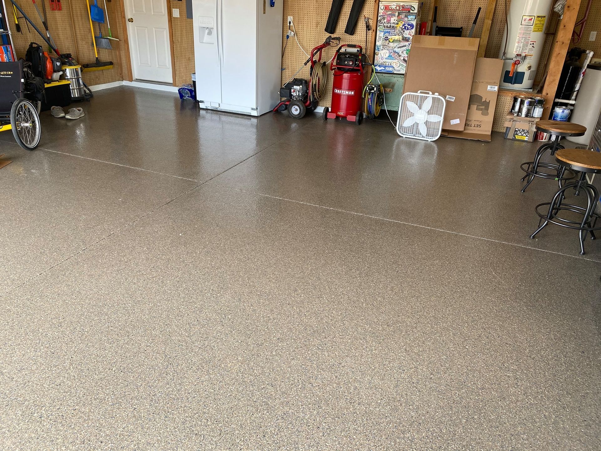 Spacious garage with a speckled epoxy floor, white refrigerator, red compressor, and stacked boxes.