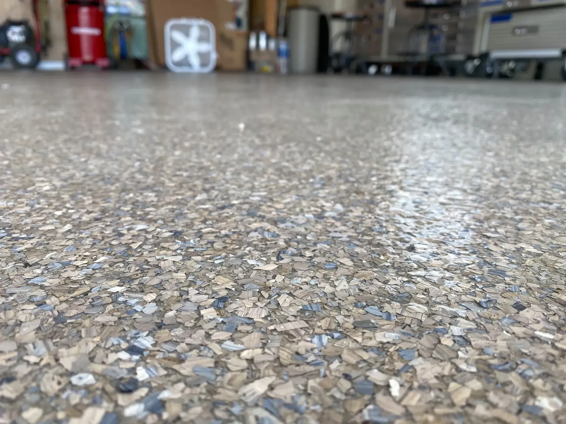 Close-up of a speckled concrete garage floor with a blurred workshop background
