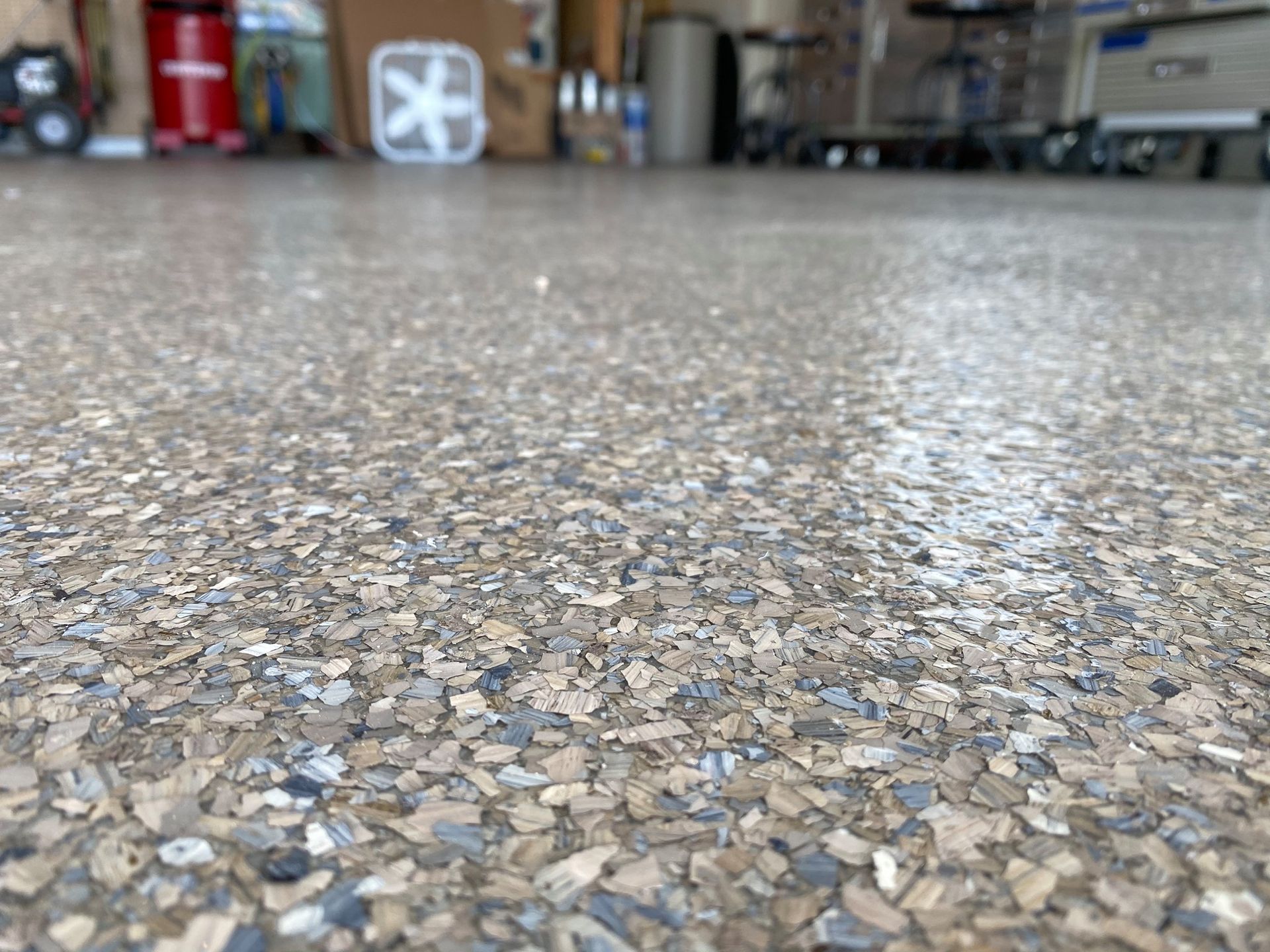Close-up of a speckled terrazzo floor in a garage or workshop, with blurred storage items in the background