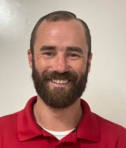 Smiling man with beard wearing a red polo shirt against a plain light background