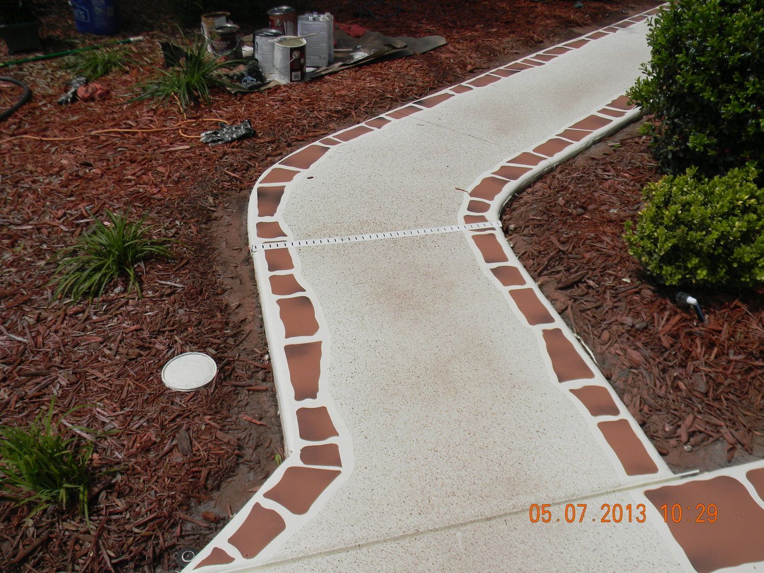 Curved white garden path with red brick edging through mulch and plants