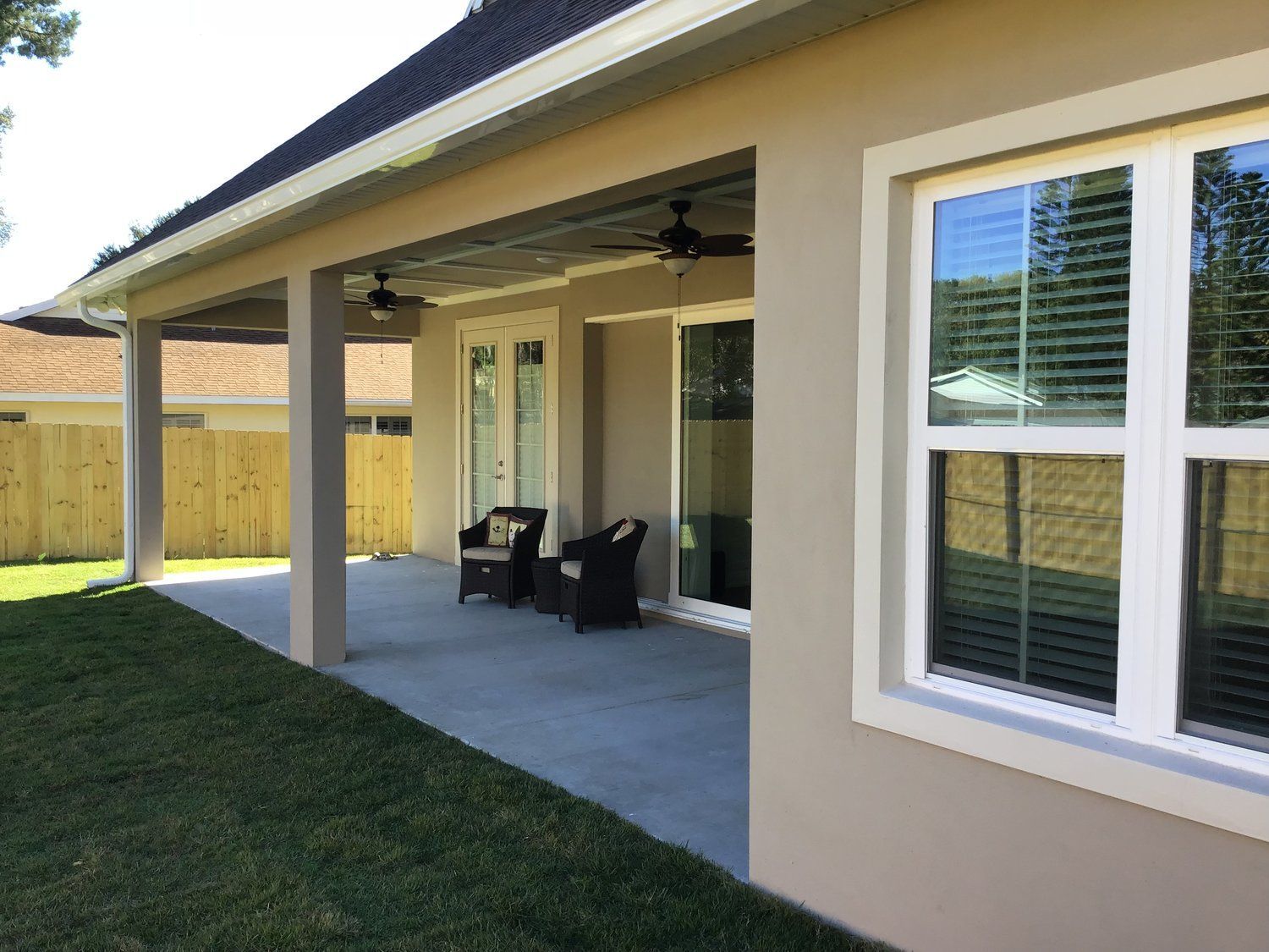 Covered patio with ceiling fans, chairs, and a window beside a grassy yard