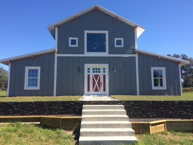 Gray barn-style building with white trim and red doors, viewed from the front with steps leading up to it