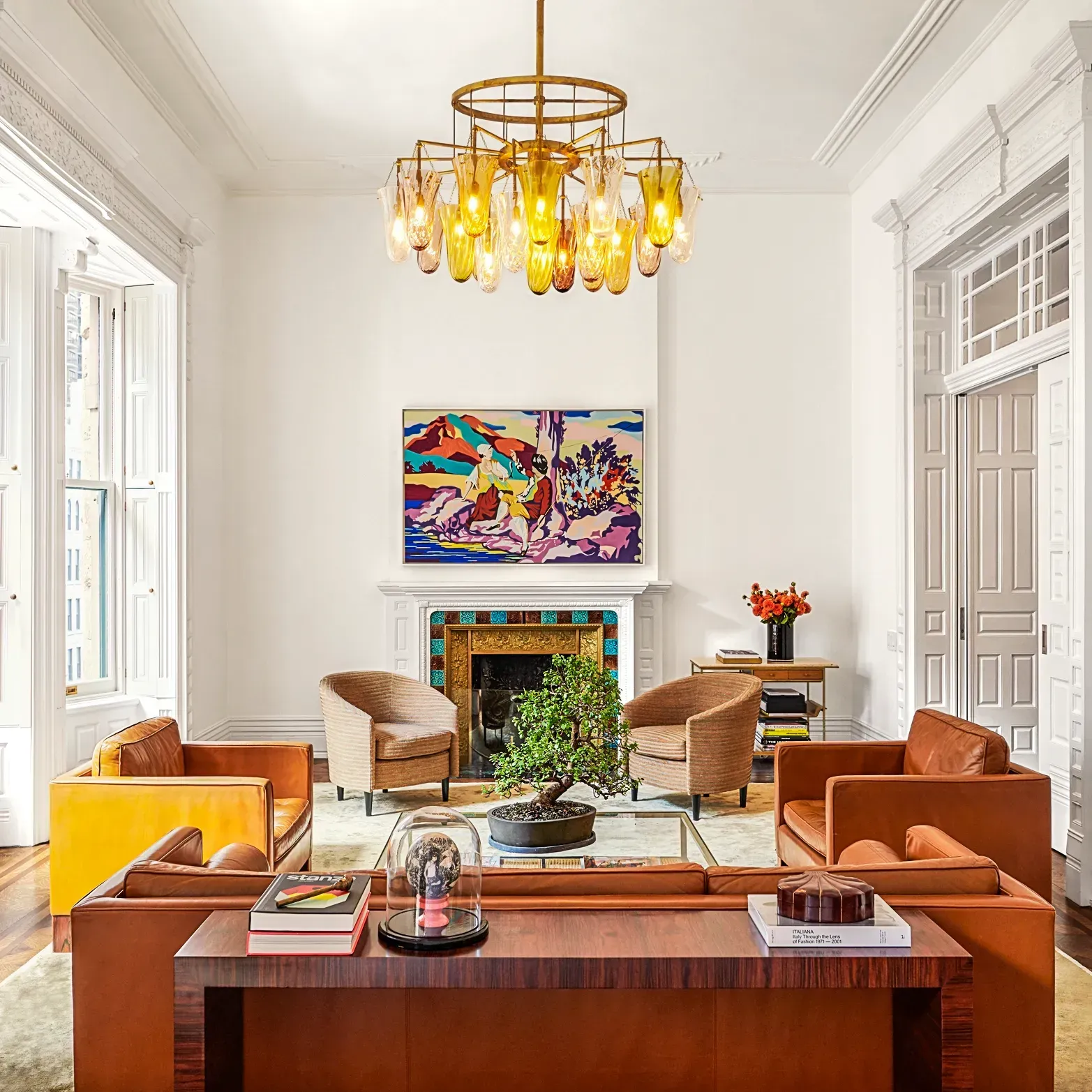 Bright living room with orange sofas, a fireplace, colorful art, and a gold chandelier.