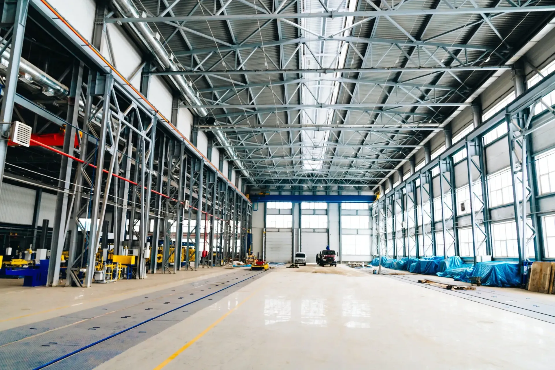 Empty industrial warehouse interior with steel beams, large windows, and a polished concrete floor