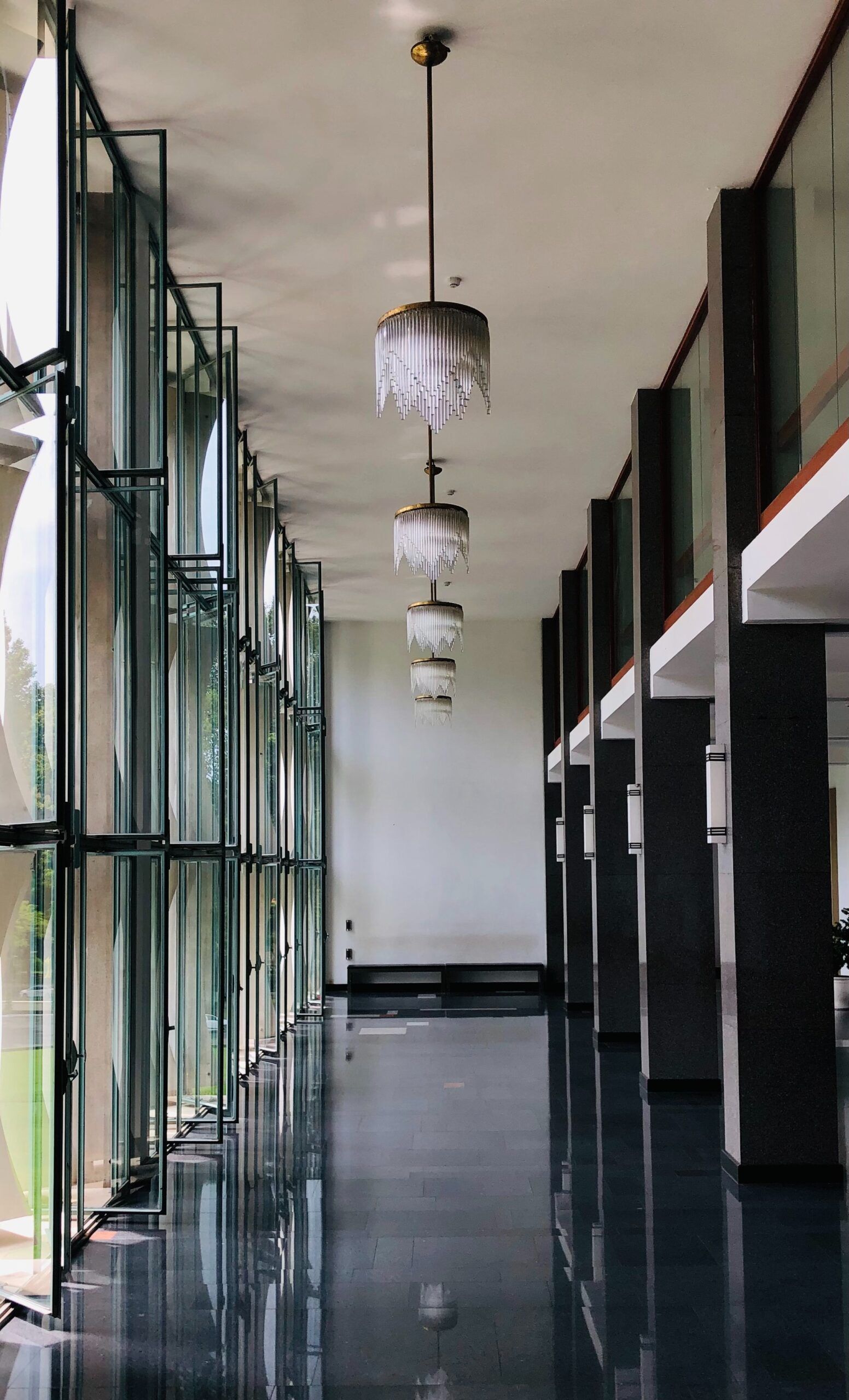 Empty hallway with black-and-white walls, glossy floor, and hanging ceiling lights